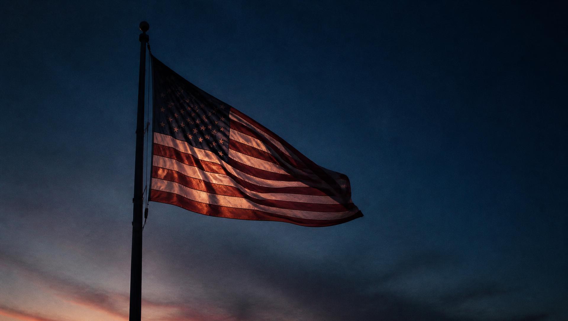 An American flag backlit against a deep blue dusk sky
